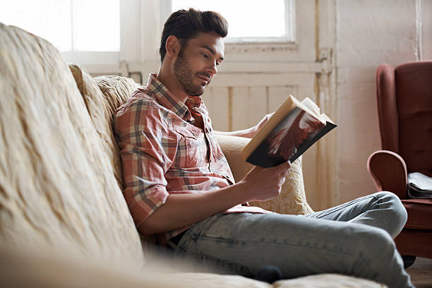 Man sitting on sofa reading a book in a cozy loft apartment